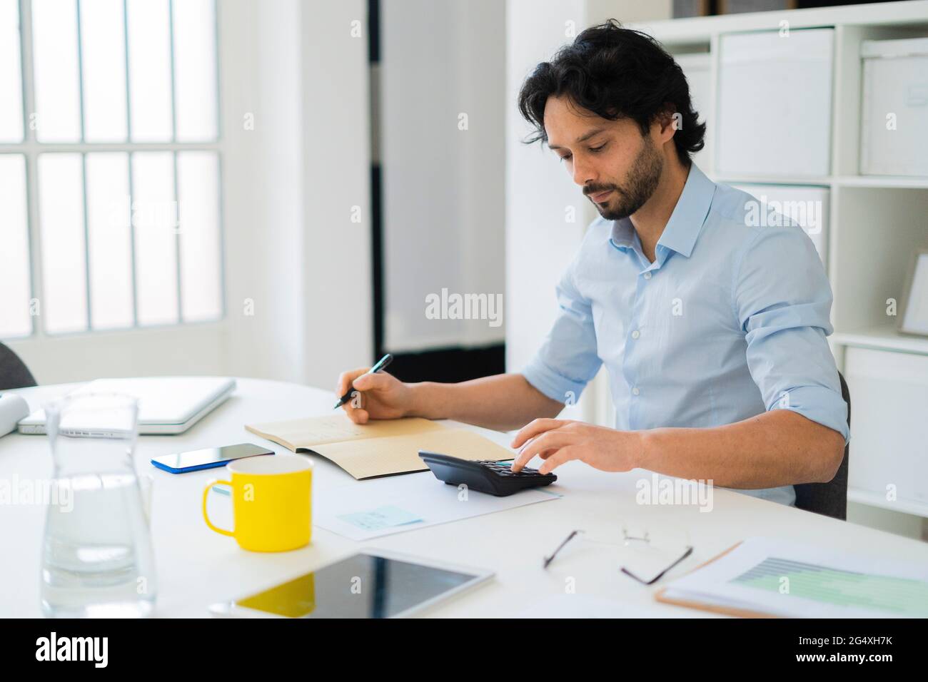 Giovane imprenditore maschile che utilizza la calcolatrice mentre lavora in ufficio Foto Stock