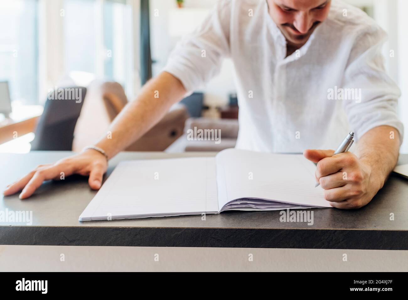 Sorridente giovane uomo che scrive sul libro all'isola della cucina Foto Stock