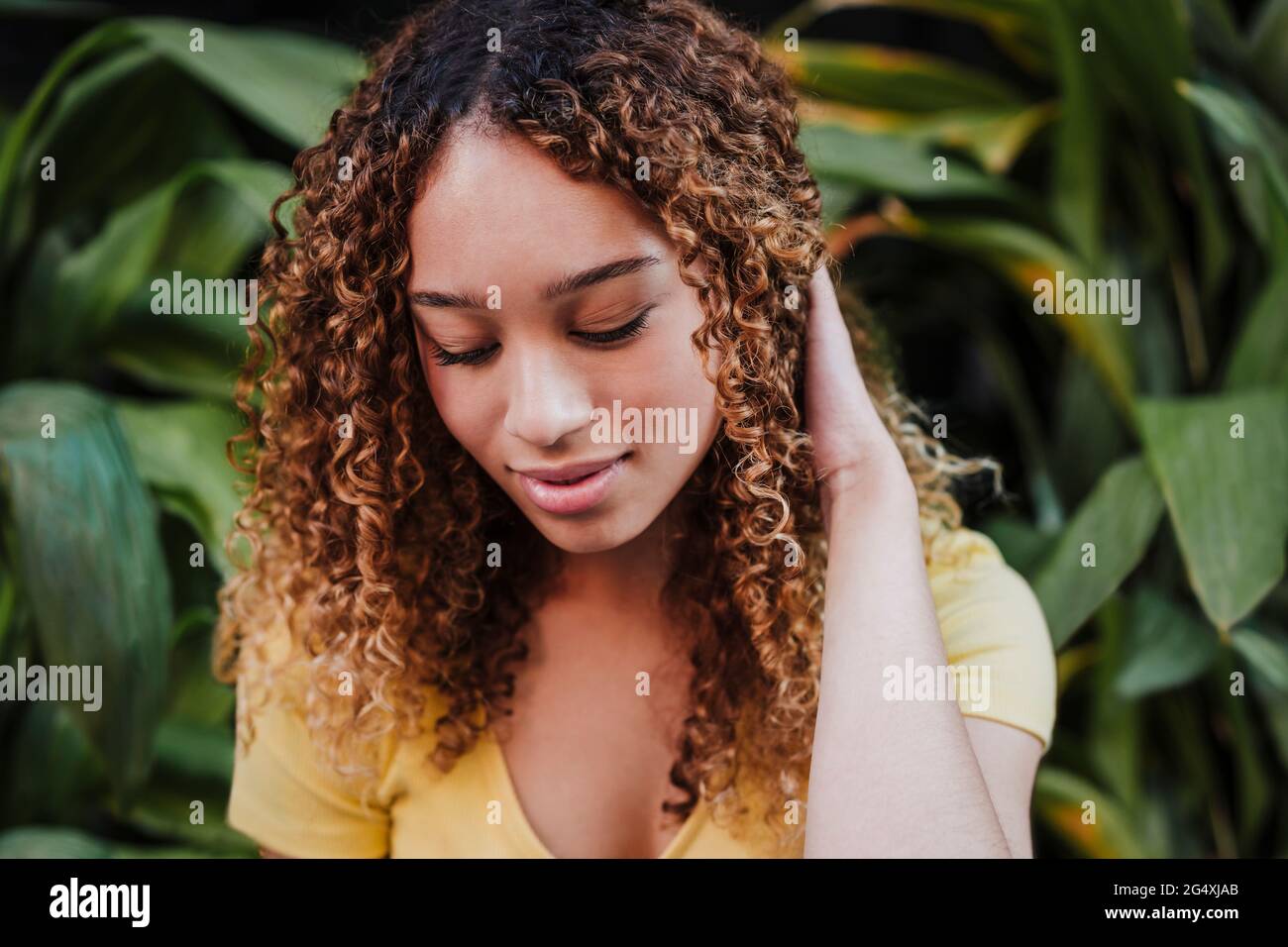 Bella donna che guarda giù con la mano nei capelli vicino alle piante Foto Stock