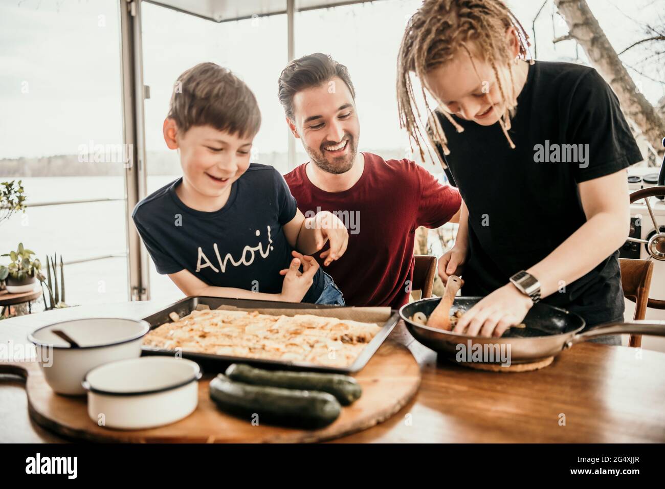 Ragazzi felici che preparano il cibo con il padre in cucina a houseboat Foto Stock