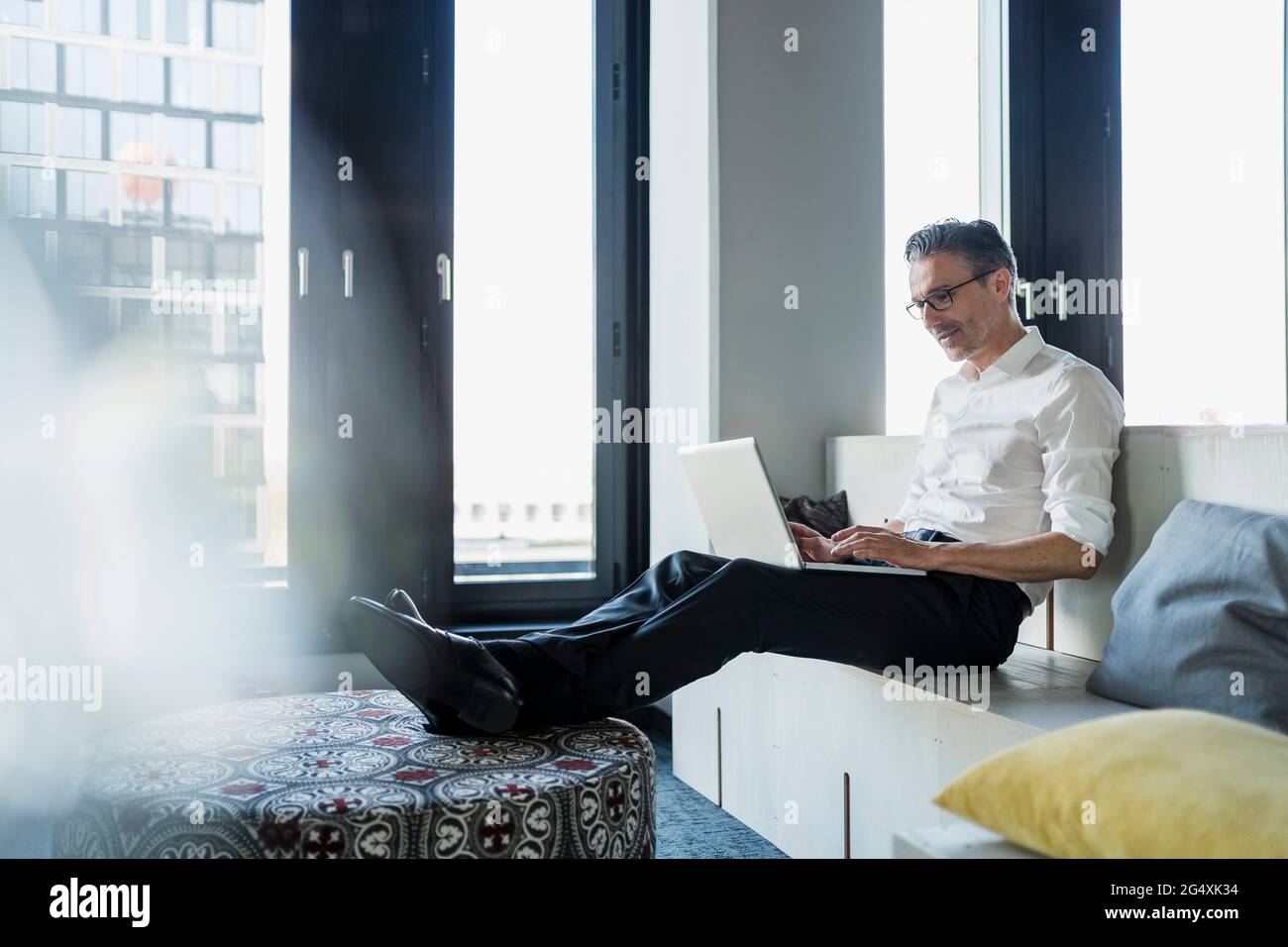 Uomo d'affari maturo che usa un computer portatile seduto su mobili mentre lavora in ufficio Foto Stock