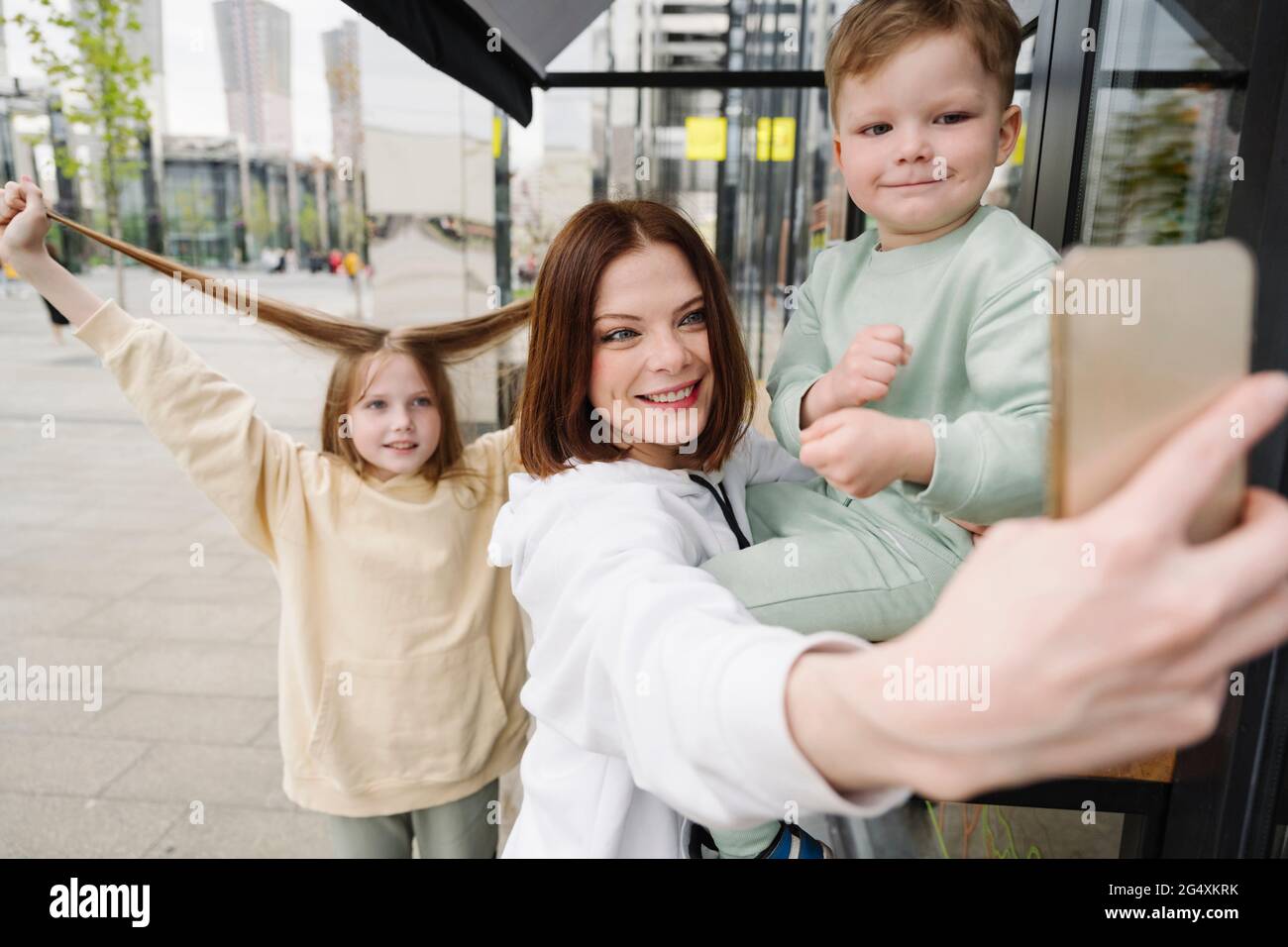 Madre sorridente che prende selfie con i bambini in città Foto Stock