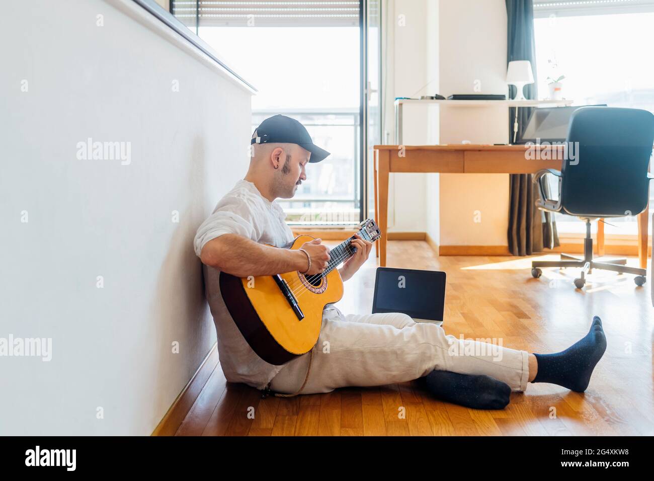 Chitarrista maschile che suona la chitarra con un computer portatile mentre  si siede a casa Foto stock - Alamy
