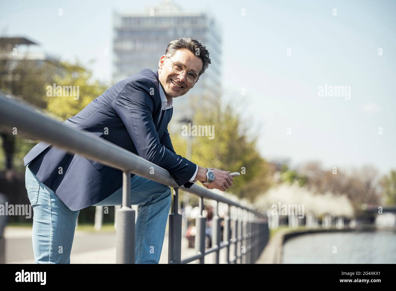 Uomo d'affari maturo sorridente mentre si appoggia alla ringhiera Foto Stock