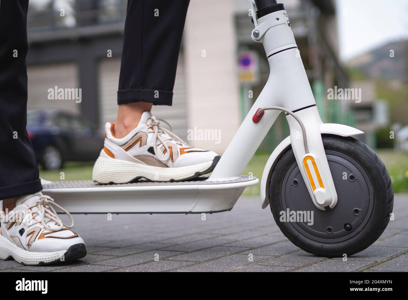 Donna d'affari che indossa scarpe sportive in piedi con scooter elettrico a spinta sul sentiero Foto Stock