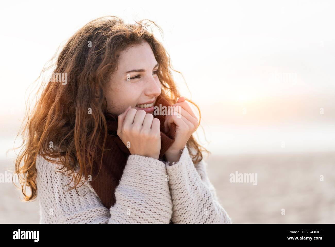 Giovane donna con testa rossa che indossa sciarpa in spiaggia Foto Stock