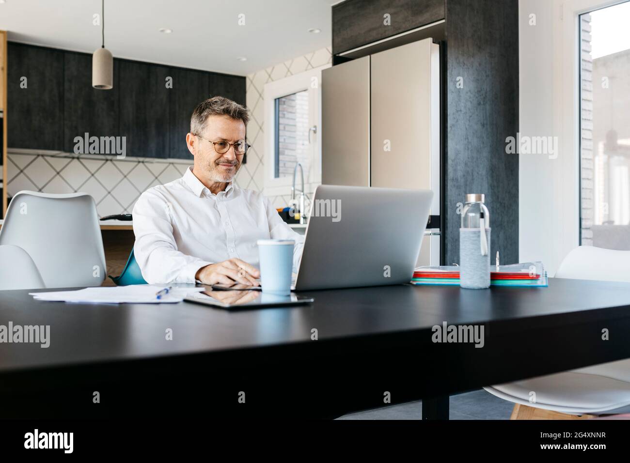 Lavoratore freelance maschile che lavora su un computer portatile in cucina a casa Foto Stock