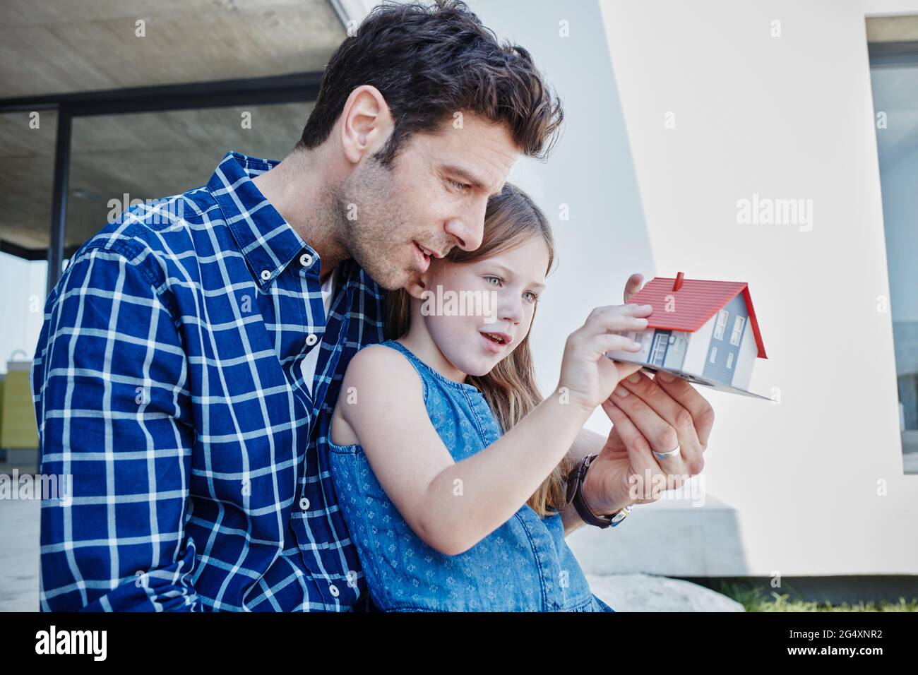 Padre seduto con la figlia che guarda il modello a casa in cortile Foto Stock