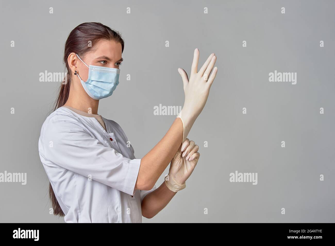 un medico in un cappotto bianco e una maschera medica mette guanti sterili in lattice bianco sulle sue mani per la procedura, spazio di copia Foto Stock