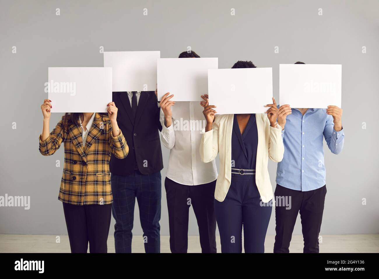 Gruppo di persone anonime che coprono i volti nascosti dietro fogli di carta bianca Foto Stock