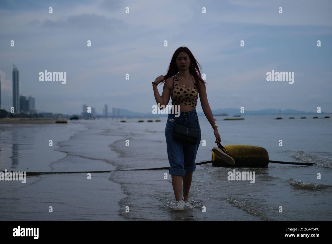 Bella donna thailandese sta camminando a piedi nudi attraverso l'acqua un po 'di bassa marea in una vista della grande città Foto Stock