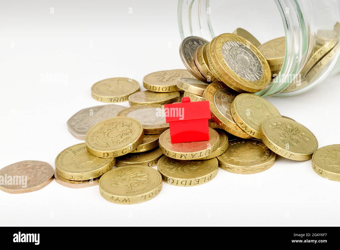 Una casa giocattolo su monete che sono fuoriuscite da un vaso da marmellata. Foto Stock