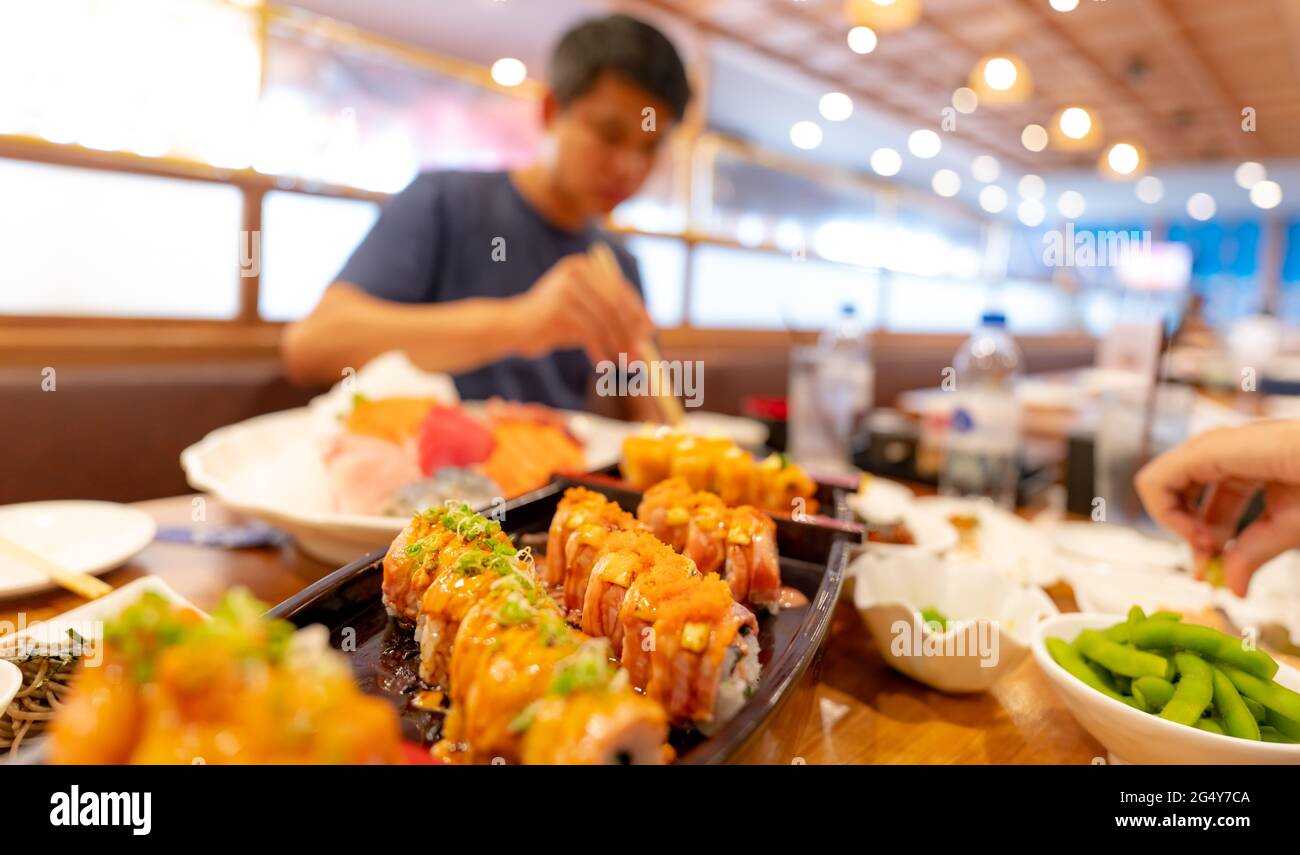 Focalizzazione selettiva sul cibo Giapponese in un ristorante Giapponese. Sushi di salmone su un piatto con l'uomo offuscato che mangia cibo giapponese con chopsticks. Foto Stock