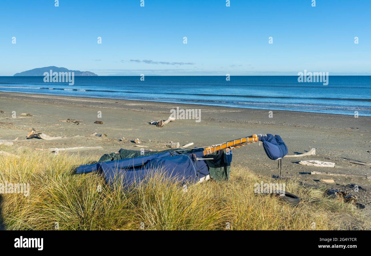 Spiaggia di Otaki con l'isola di Kapiti sullo sfondo con uno yacht in canoa coperto sulla spiaggia. Foto Stock