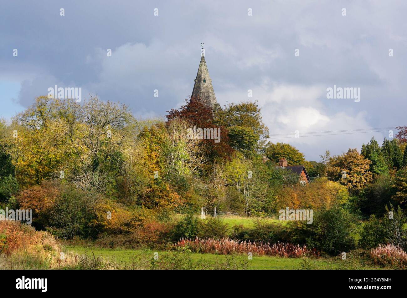 Chiesa di San Ciad a Longsdon, Staffordshire. Guglia della Chiesa che domina gli alberi e i campi d'autunno in un idillio rurale. Foto Stock