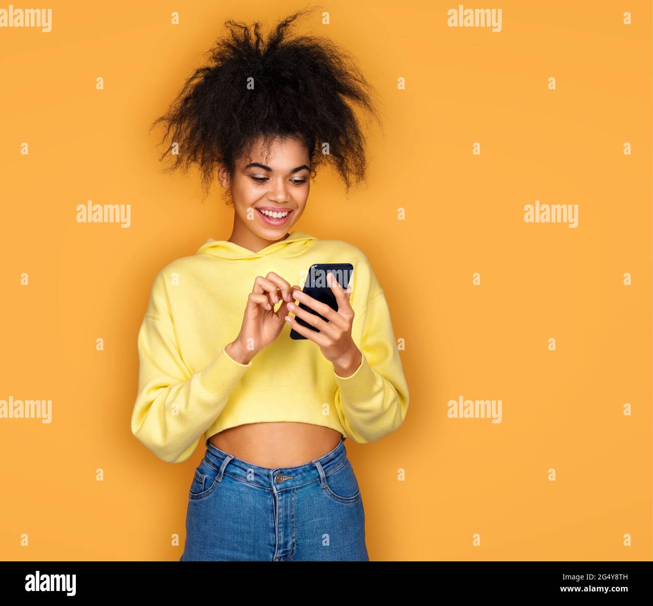 La ragazza usa il telefono, controlla la presenza di nuovi messaggi. Foto di ragazza afroamericana su sfondo giallo Foto Stock