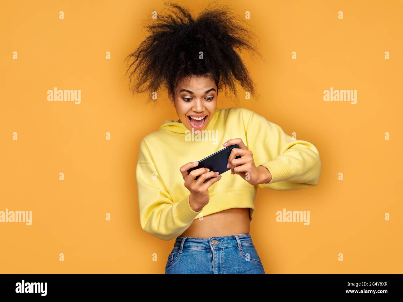 La ragazza si è divertita con lo smartphone, giocando a videogame. Foto di ragazza afroamericana su sfondo giallo Foto Stock