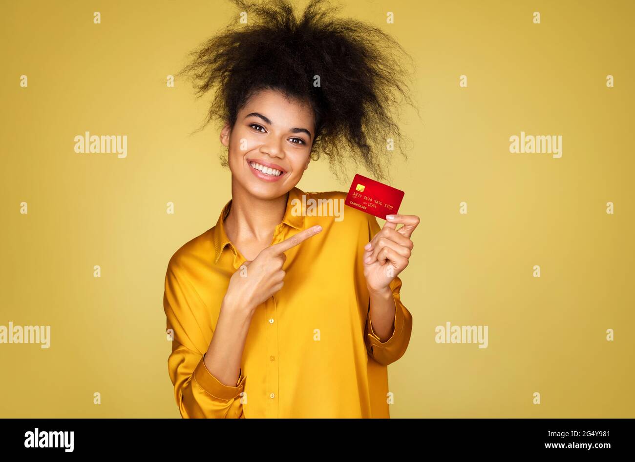 La ragazza si è addentata con un dito sulla carta di credito. Foto di ragazza afroamericana su sfondo giallo Foto Stock