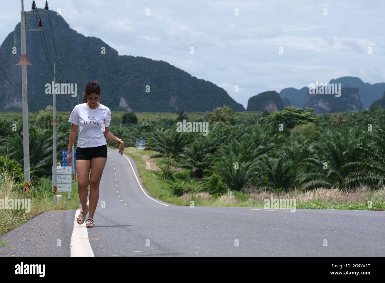 Una bella donna thailandese cammina su una strada che conduce a una montagna verde all'orizzonte Foto Stock