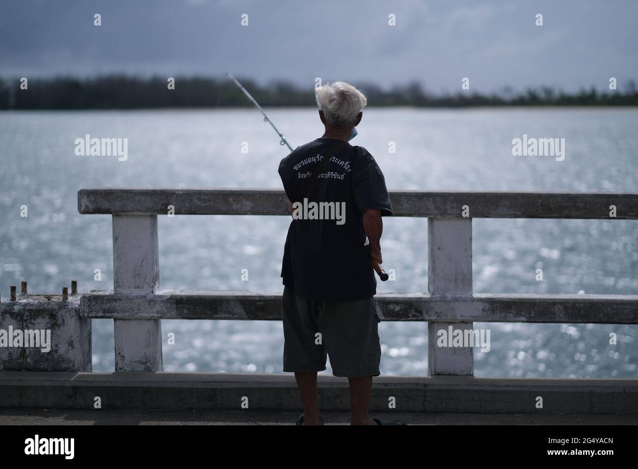 Un uomo thailandese anziano sta pescando da un ponte alto Foto Stock