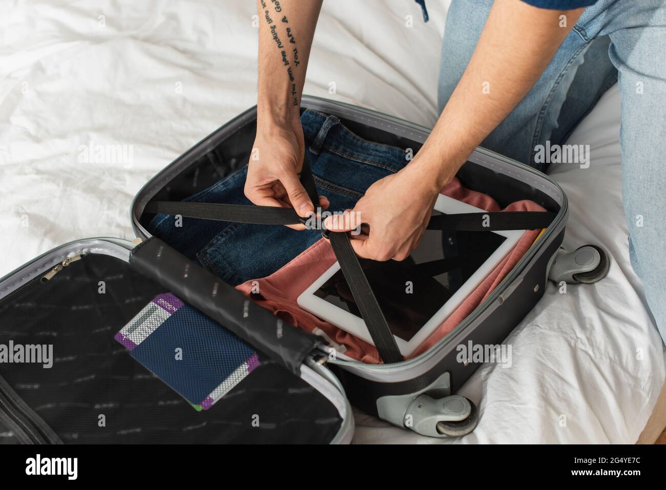 Vista ritagliata delle scommesse turistiche di chiusura della valigia con tablet digitale e passaporto sul letto Foto Stock