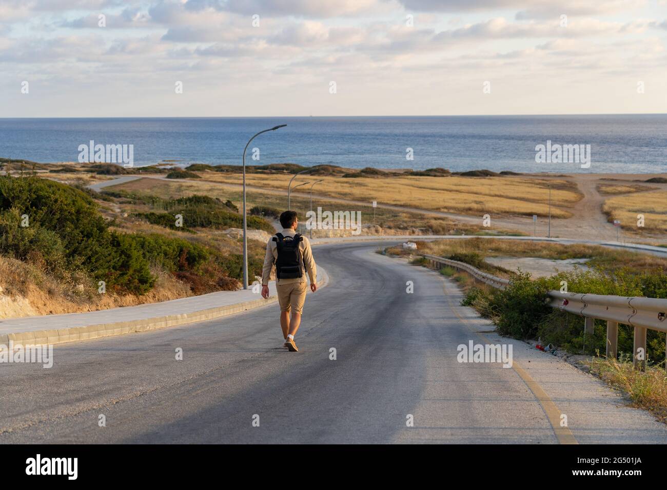 Uomo turistico con zaino passeggiate in montagna lungo strada asfaltata verso il mediterraneo a cipro nella zona di Agios Georgios Pegeias. Vista posteriore di Foto Stock