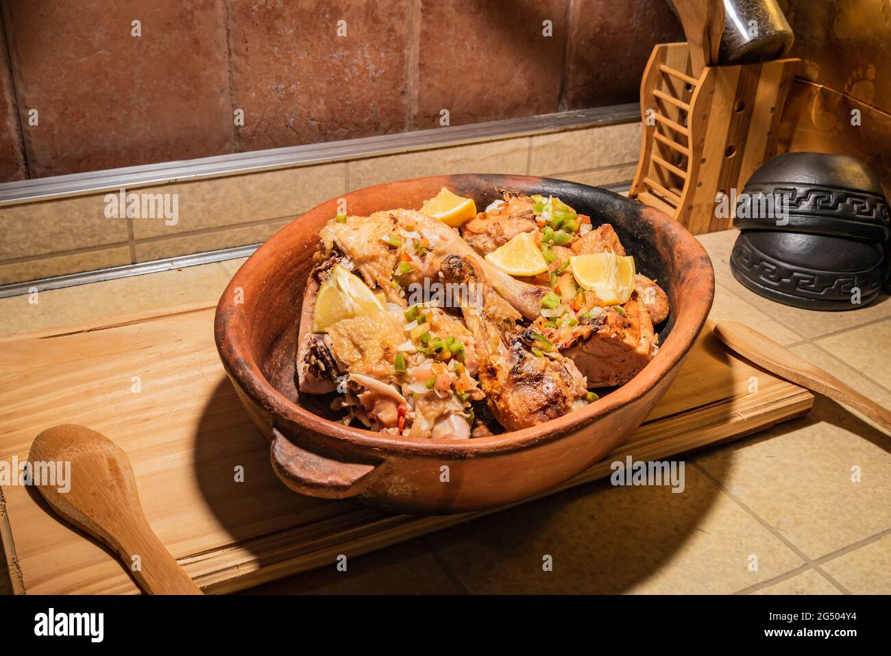 Pollo alla griglia fatto in casa con spezie tagliate a pezzi in teglia rossa in ceramica su tavola di legno. Foto Stock