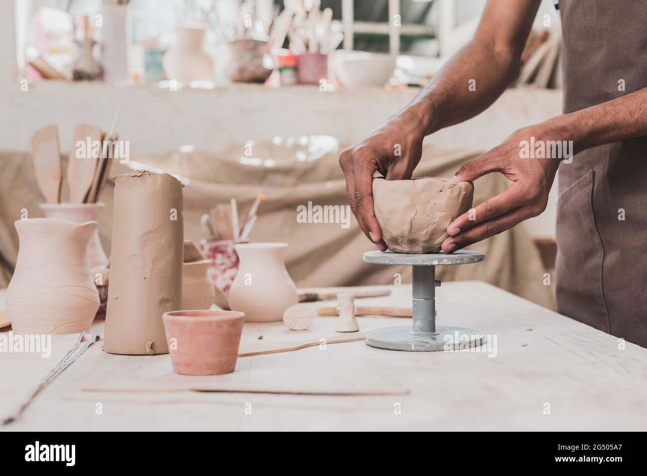 vista parziale del giovane afroamericano che sculpina di argilla con le mani sul tavolo con attrezzatura in ceramica Foto Stock vista parziale del giovane afroamericano che sculpina di argilla con le mani sul tavolo con attrezzatura in ceramica Foto Stock
