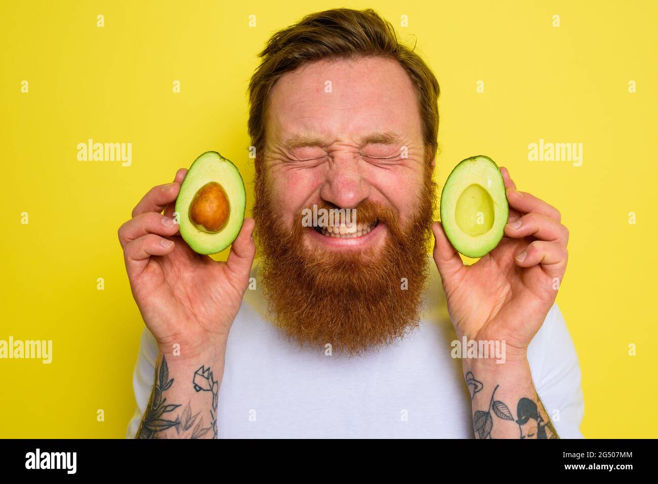 L'uomo felice con barba e tatuaggi tiene un avocado Foto Stock