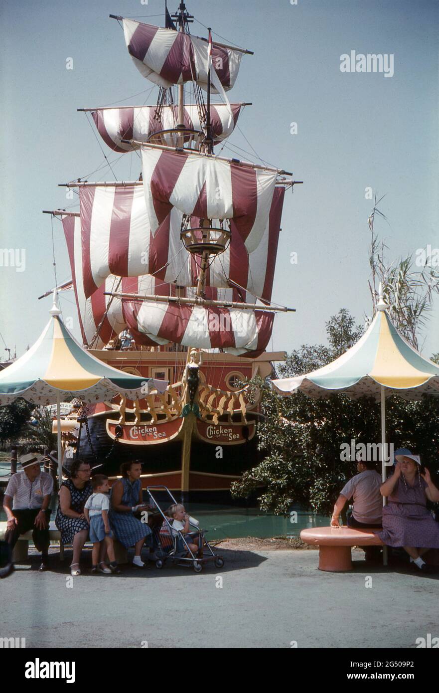 Disneyland, California, 1959. Una vista del ‘Pollo del Mare’ Capitano Hook’s Pirate Ship Restaurant a Fantasyland, con le sue vele a strisce sfurtate. I visitatori si riposano e si riparano sotto gli ombrelloni. Foto Stock