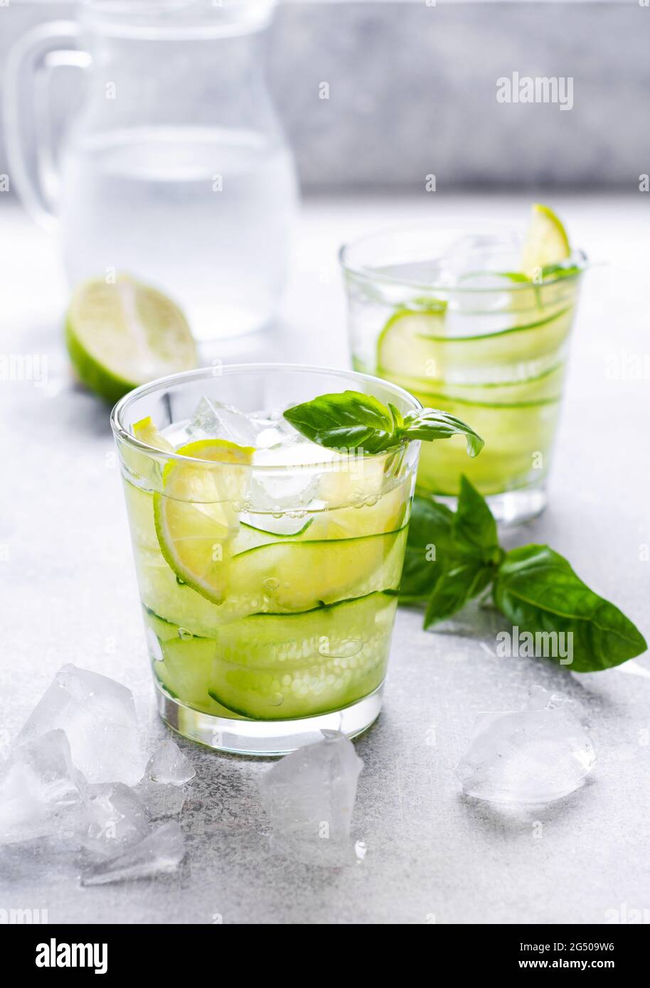 Rinfrescante limonata estiva fatta in casa da lime, limone, cetriolo e basilico con ghiaccio in vetro su vecchio fondo di cemento. Messa a fuoco selettiva. Foto Stock