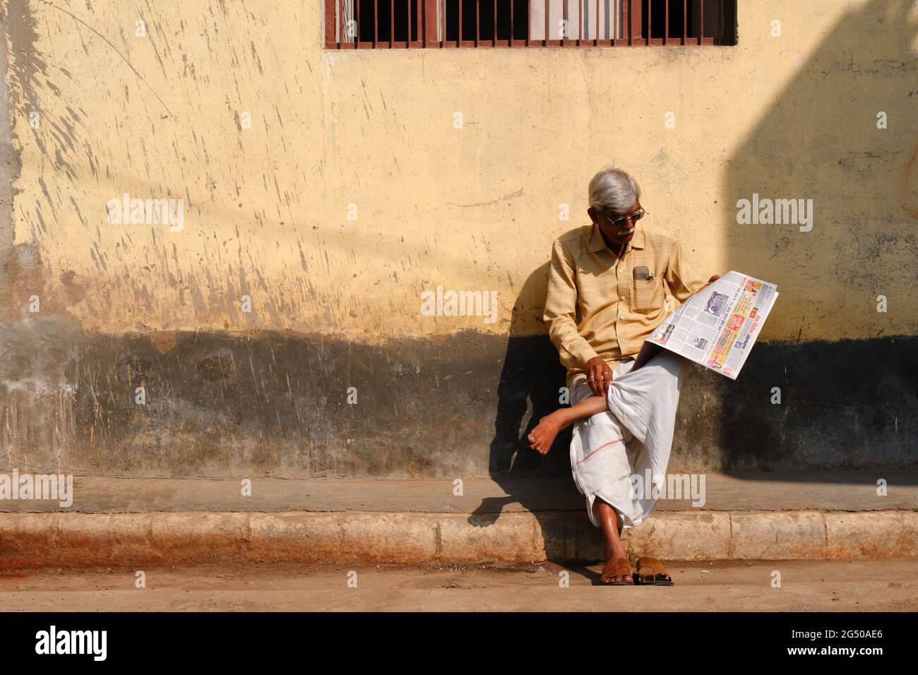 VARANASI, INDIA - 04 febbraio 2021 : Unidentified Man siede comodamente e legge giornale indiano sulla strada di Varanasi Foto Stock