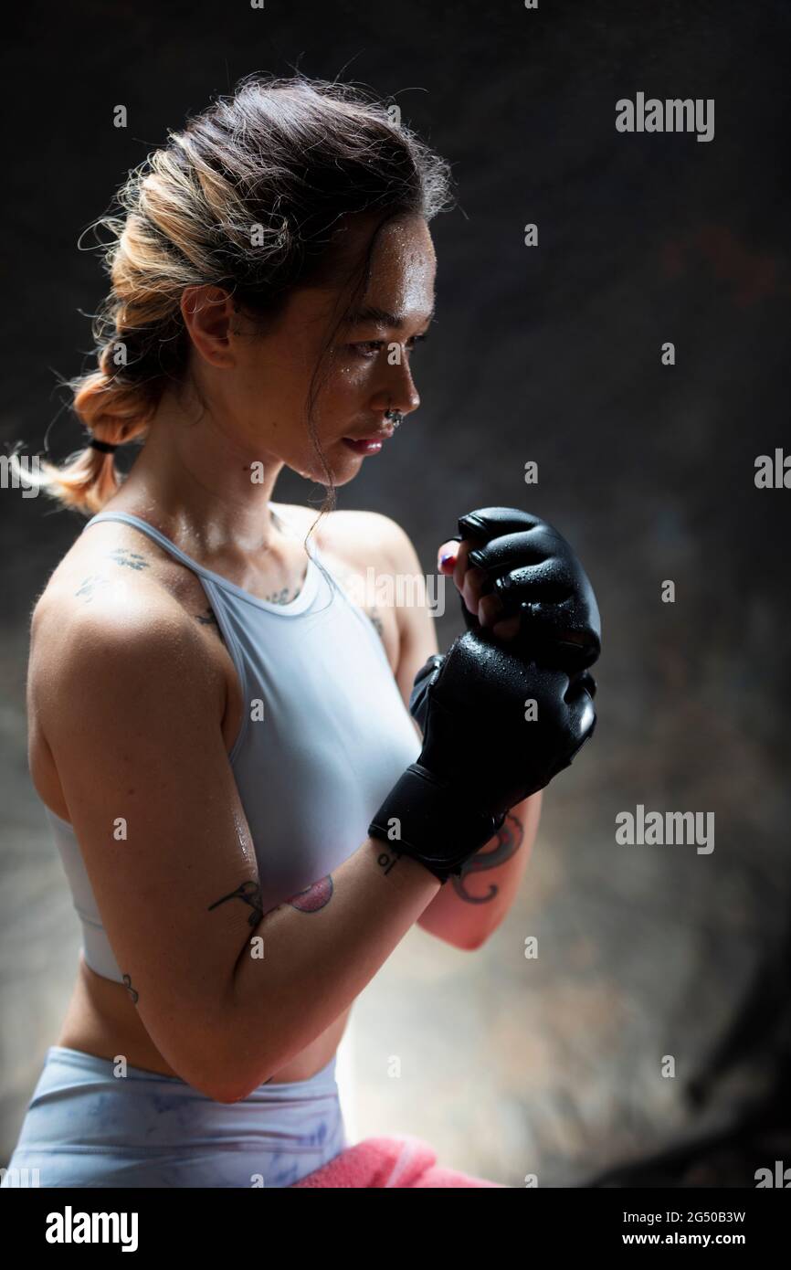 Vista laterale di una giovane donna che indossa guanti da boxe, guardando di fronte a lei. Ha i suoi pugni in su ed è pronta a combattere. Foto Stock