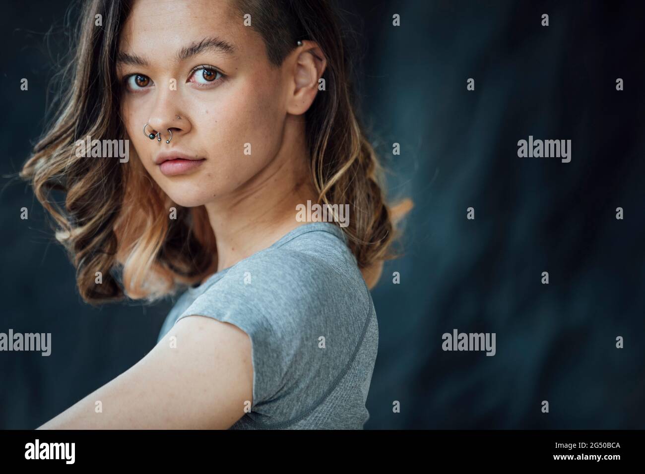 Una giovane donna contenta e trendy che posa per la telecamera. È in piedi davanti a uno sfondo. Foto Stock