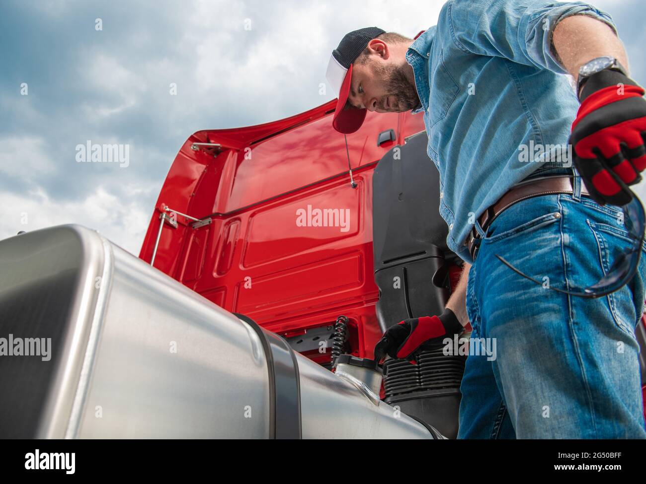 Conducente di semi-camion caucasico nei suoi 30 anni guardando il tappo del serbatoio diesel alla ricerca di perdite o di carburante diesel rubato. Tema industria dei trasporti. Foto Stock