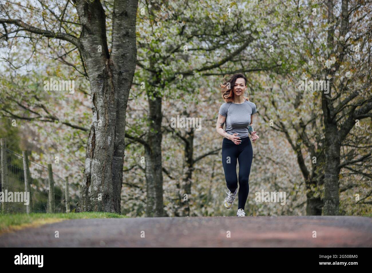Una giovane donna che indossa il gymwear, sta facendo jogging nel parco, sotto alberi di fiori. Foto Stock