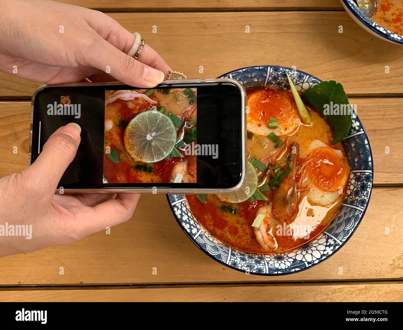 Donna che scatta foto della ciotola di Tom Yum Kung noodle sul suo smartphone da condividere sui social network. Tom Yum Kung è il cibo tailandese popolare Foto Stock