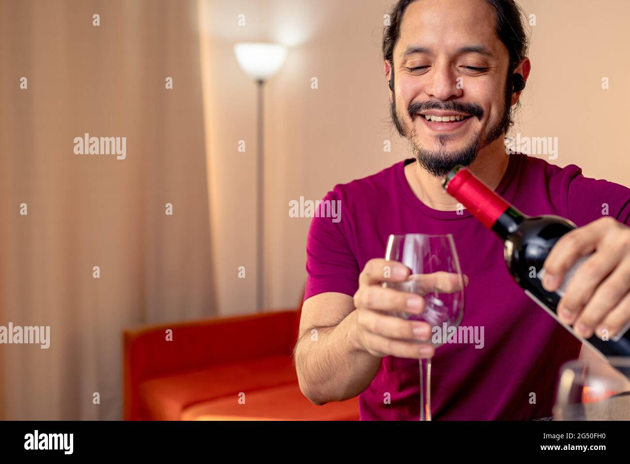 Giovane latino che beve vino rosso a casa in soggiorno Foto Stock