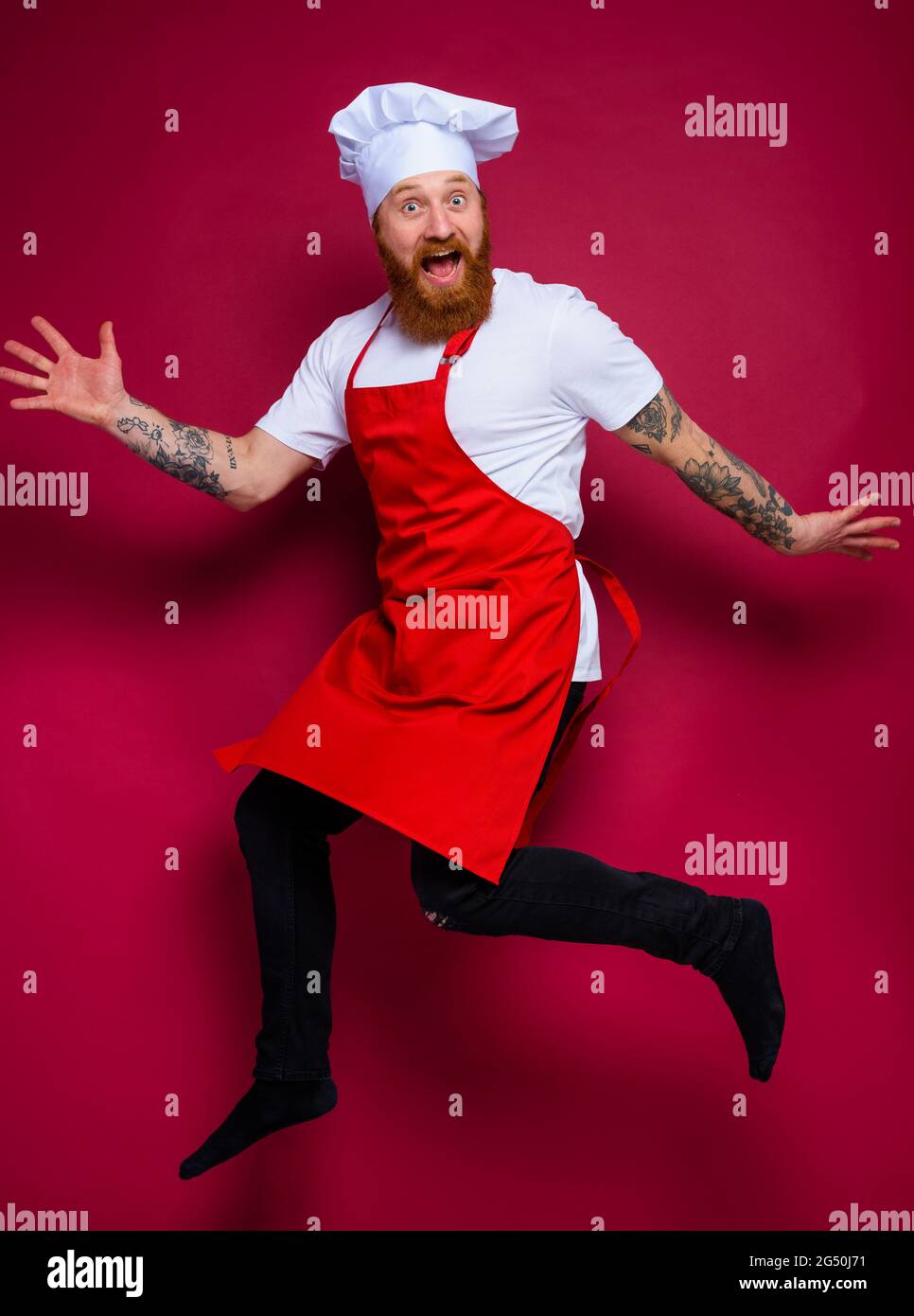 chef felice con barba e grembiule rosso salti Foto Stock