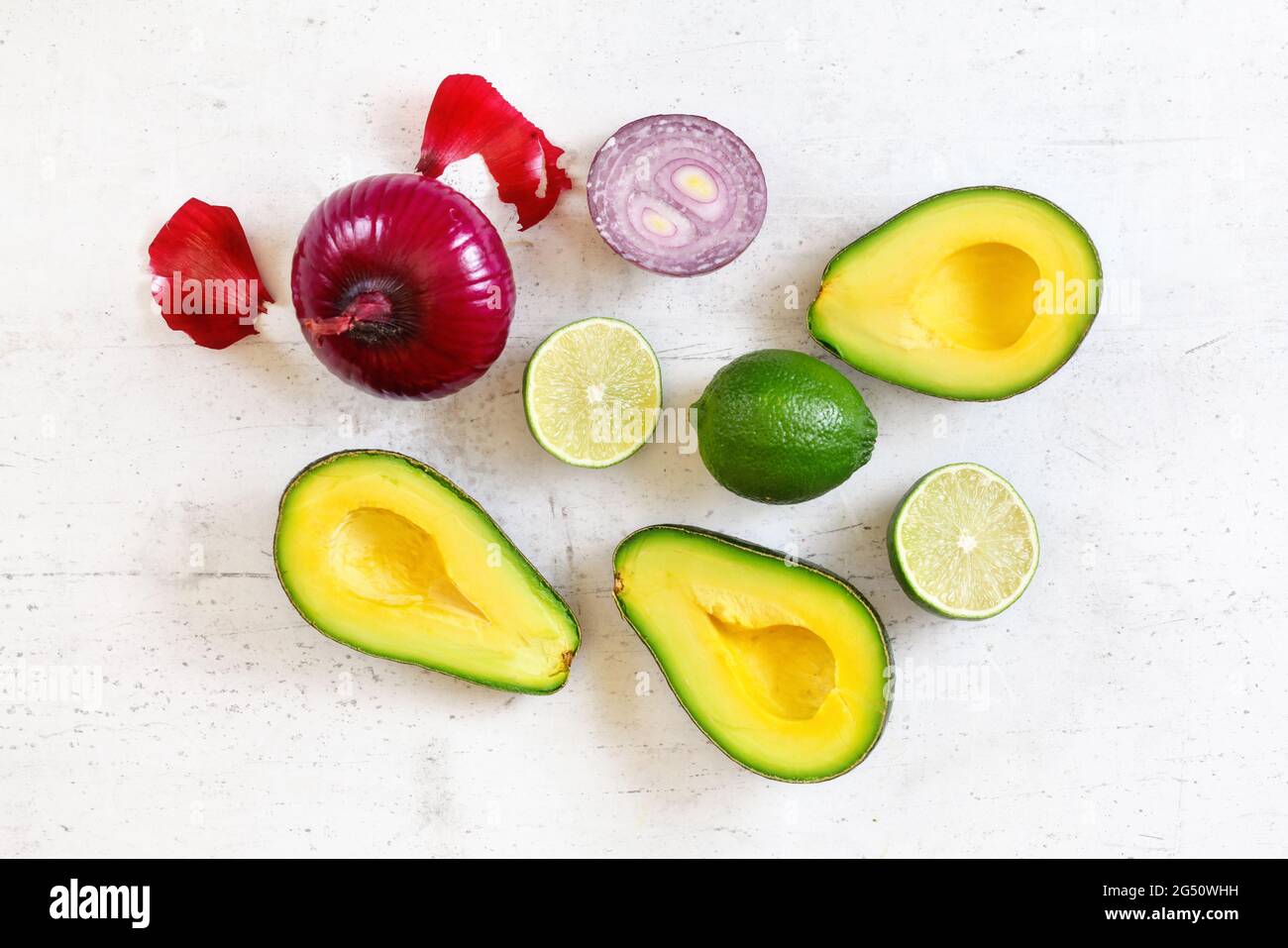 Metà avocado, lime e cipolle - ingredienti base guacamole su tavola da lavoro bianca, foto piatta Foto Stock