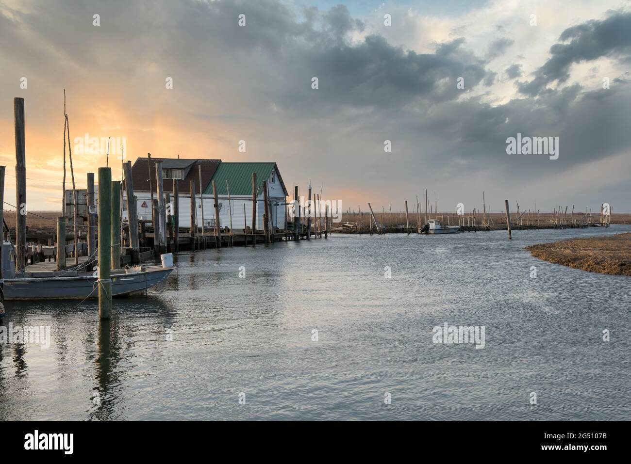 Zona di pesca con esca casa e ristorante, con un cielo drammatico, molo, acqua e terra. Foto Stock