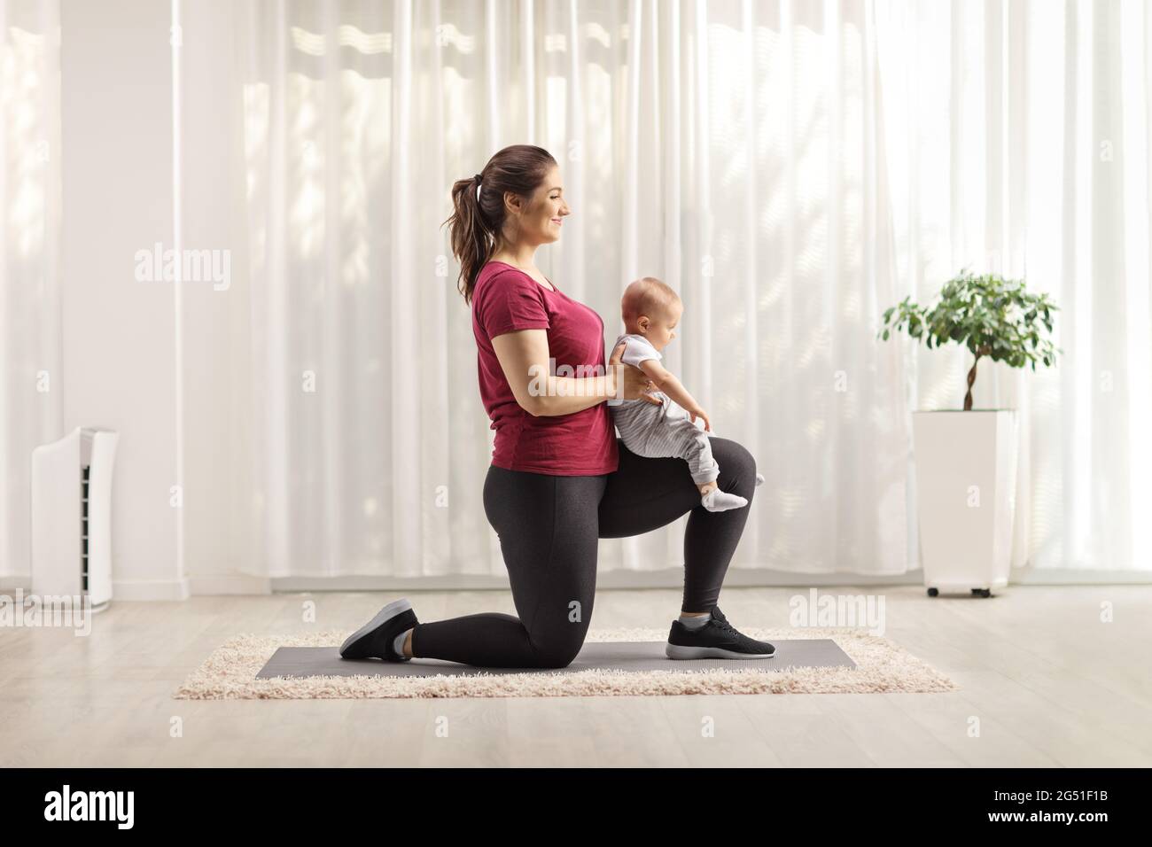 Madre giovane che si inginocchiano, si esercita e tiene un bambino all'interno Foto Stock