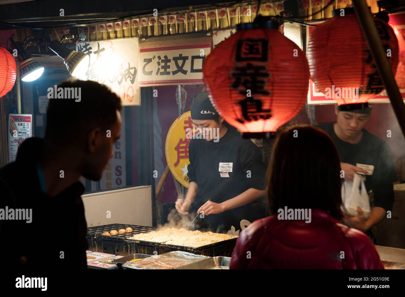 Una donna che fa il takoyaki ad una bancarella di cibo a Dotonbori, Osaka, Giappone Foto Stock