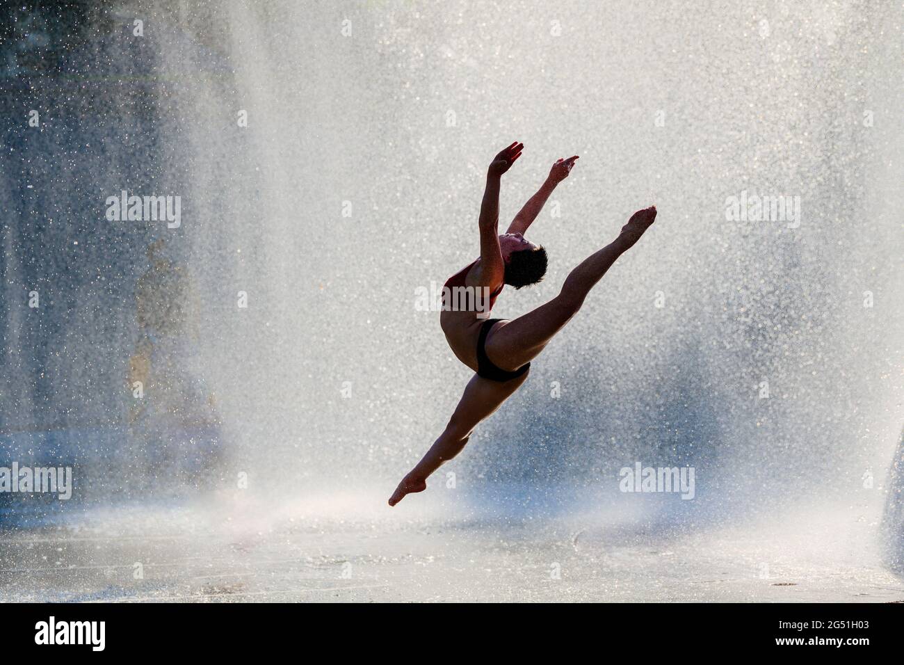 Silhouette di donna che fa acrobatica saltando posa contro fontana Foto Stock