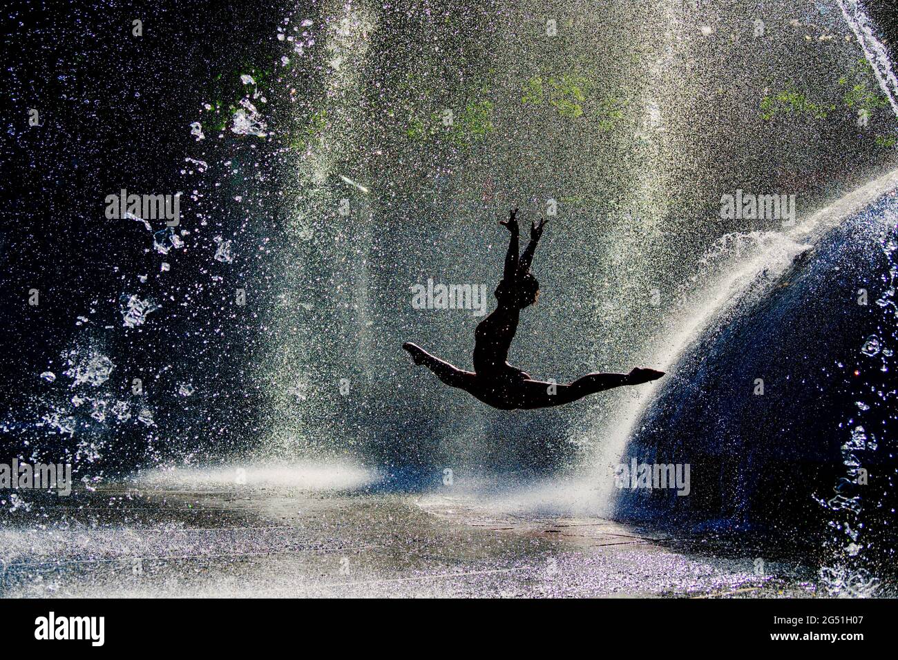 Silhouette di donna che fa acrobatica saltando posa contro fontana Foto Stock