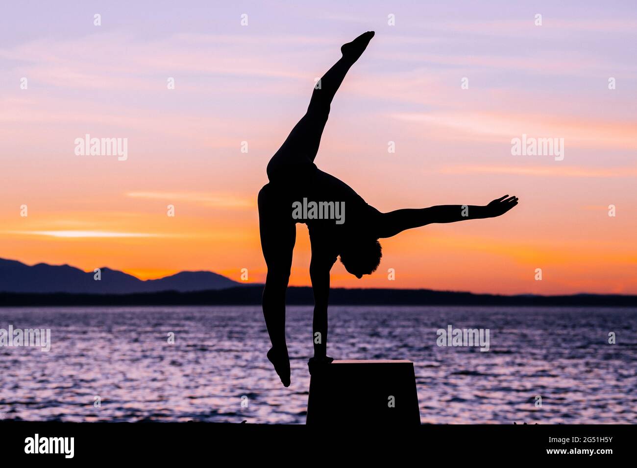 Silhouette di donna che fa la posa acrobatica contro il mare al tramonto Foto Stock