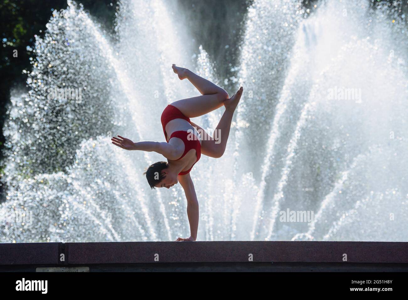 Donna che fa il supporto acrobatico posa contro la fontana Foto Stock