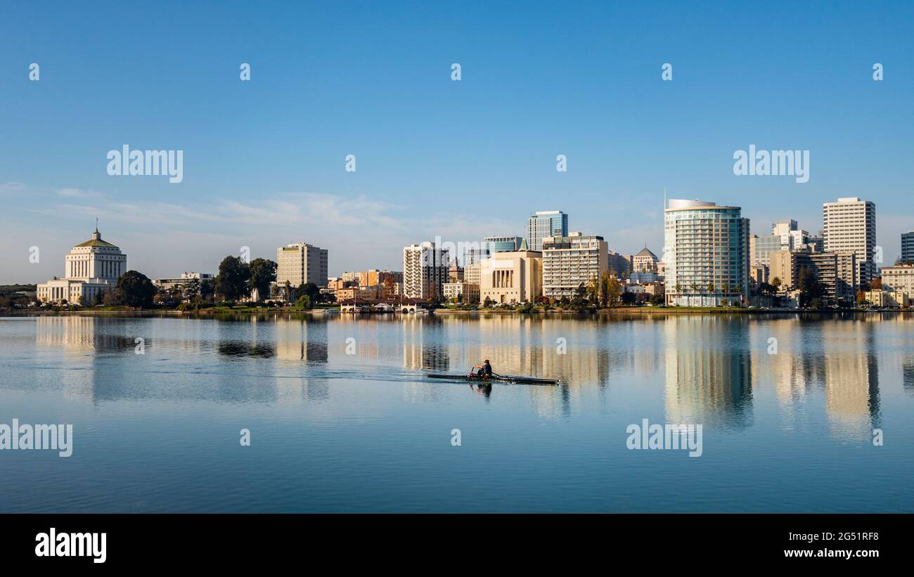 Uomo che canottava in barca sul lago Merritt con lo skyline di Oakland sullo sfondo, California, Stati Uniti Foto Stock