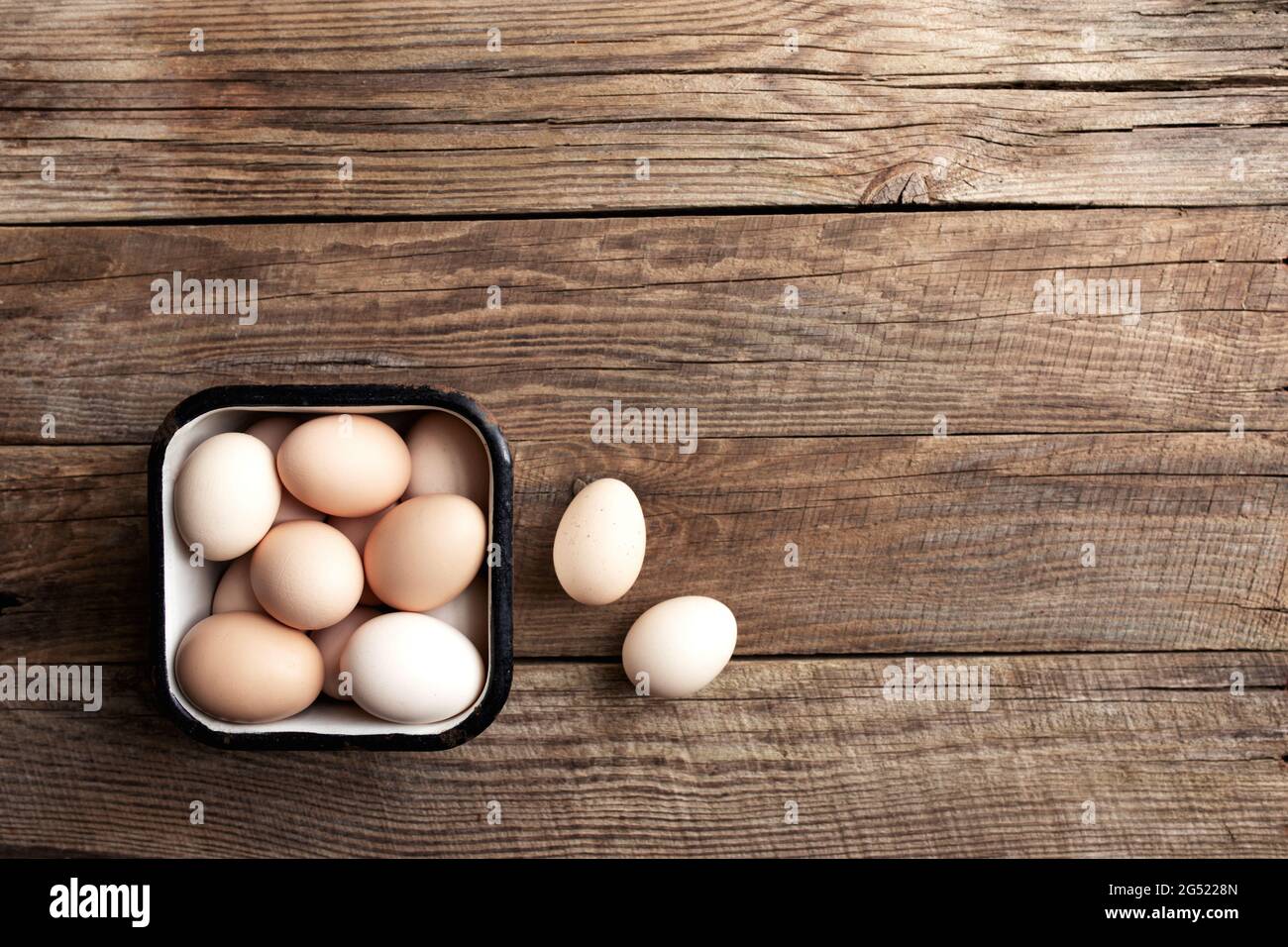 Piatto con cestello in metallo pieno di uova di pollo biologiche su sfondo di legno. Concetto domestico biologico con uova da free-range e rais pascolo Foto Stock