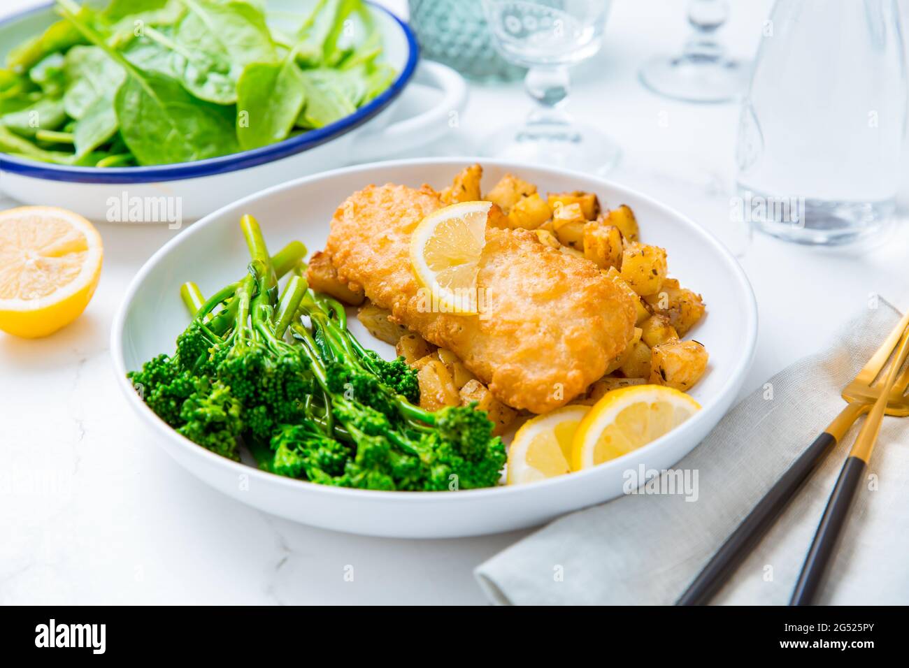Filetto di fisch impanato con patate piccanti al forno e insalata di broccoli (bimi) con limone Foto Stock